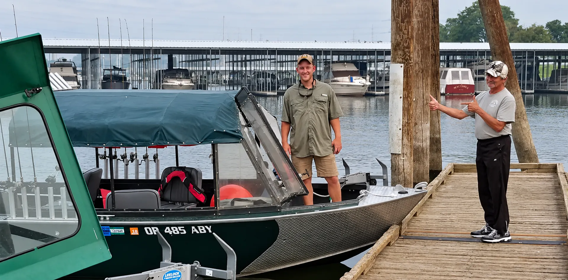 Two guides at a marina dock beside a green Alumaweld guide boat with a covered, enclosed cabin and rod holders
