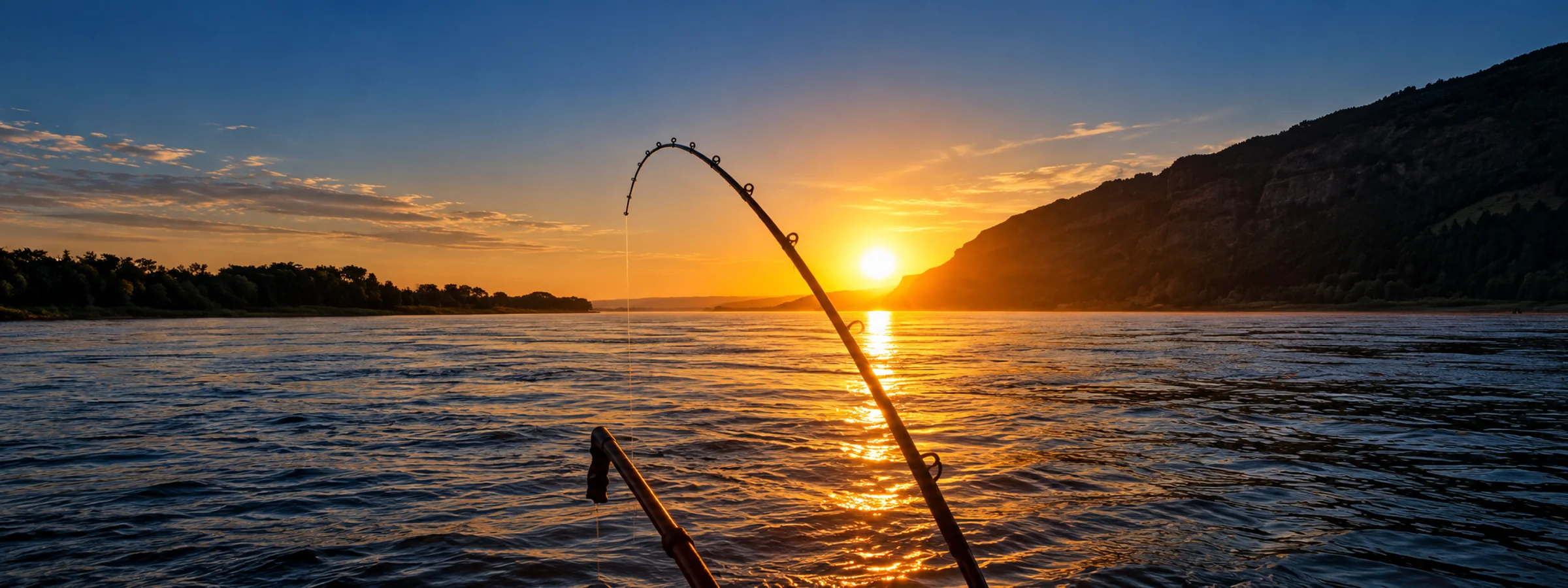 Bent fishing rod silhouetted over the Columbia River as the low sun lights the water beside the cliffs