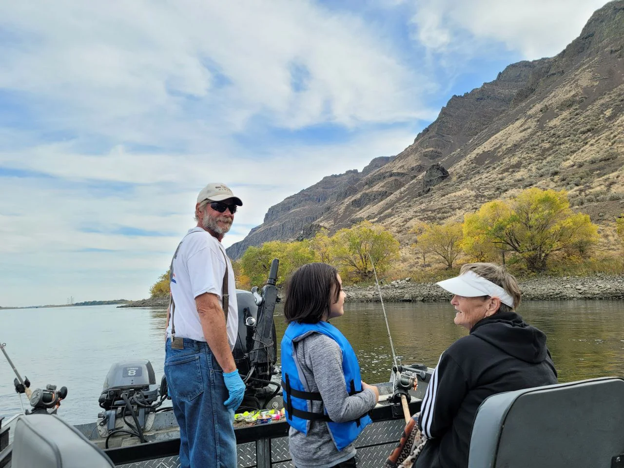 Guide and two guests chatting on the boat deck with basalt cliffs and yellow trees behind them