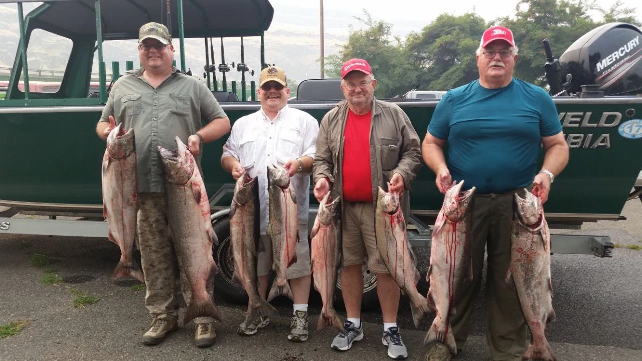 Four anglers each holding two Chinook salmon in front of the green guide boat