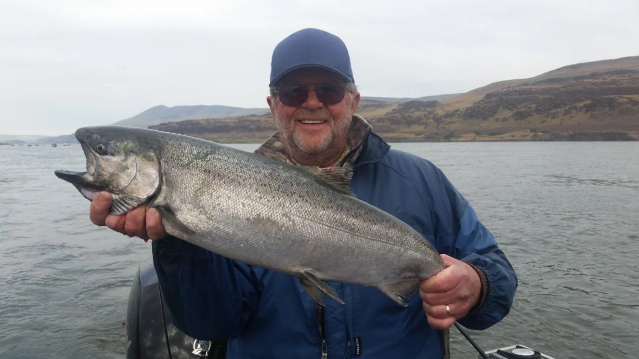 Angler in a blue jacket holding a Chinook salmon over calm water