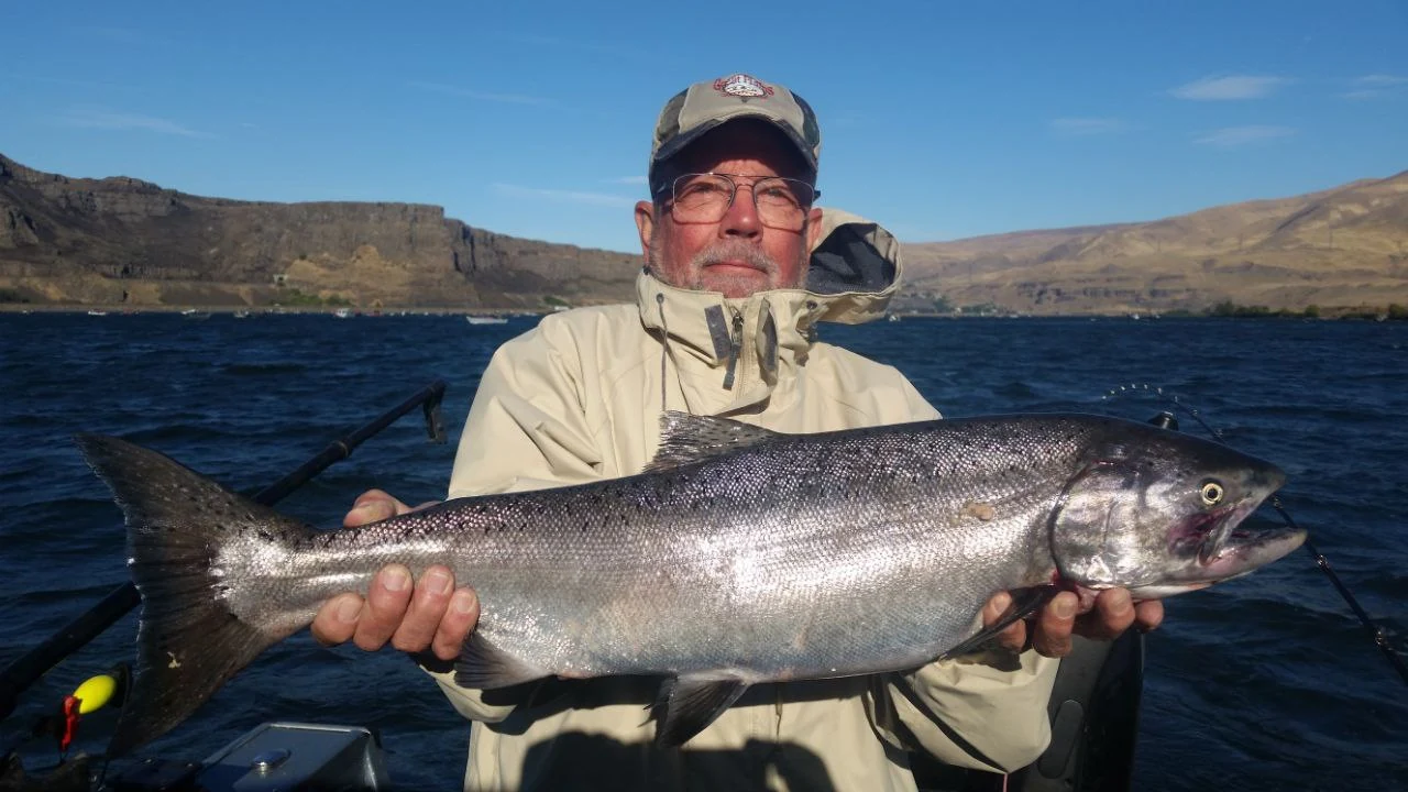 Angler holding a Chinook salmon with brown hills behind him