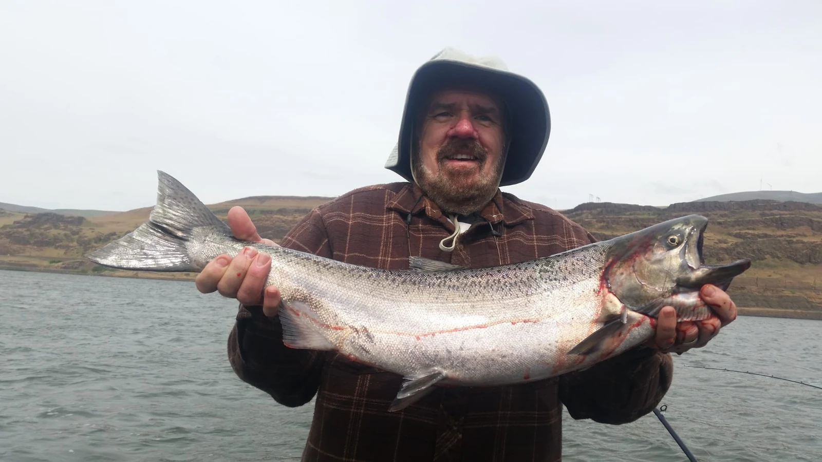Man in a plaid shirt and bucket hat holding a Chinook on the river