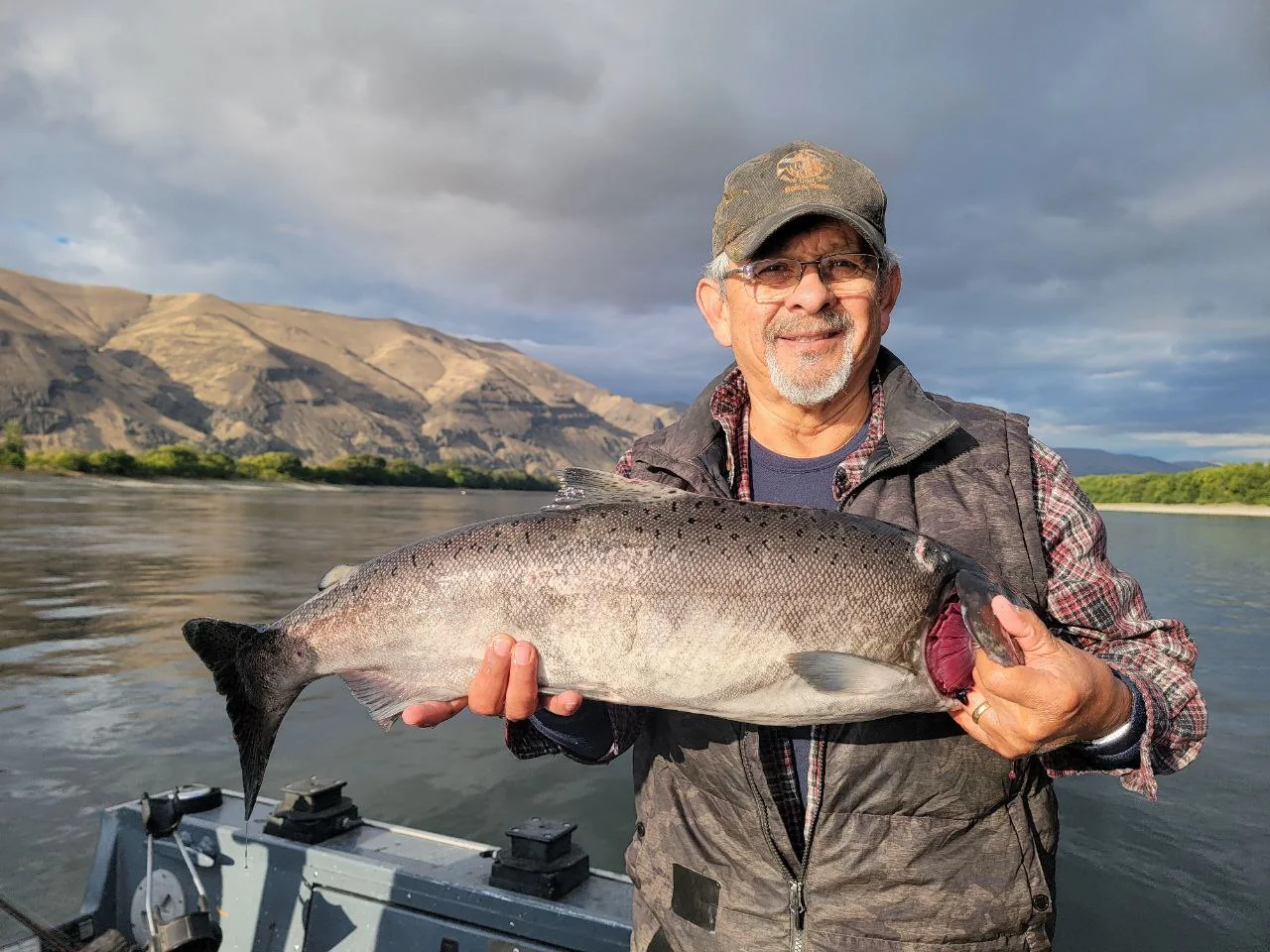 Man in a plaid vest holding a big Chinook under a cloudy sky