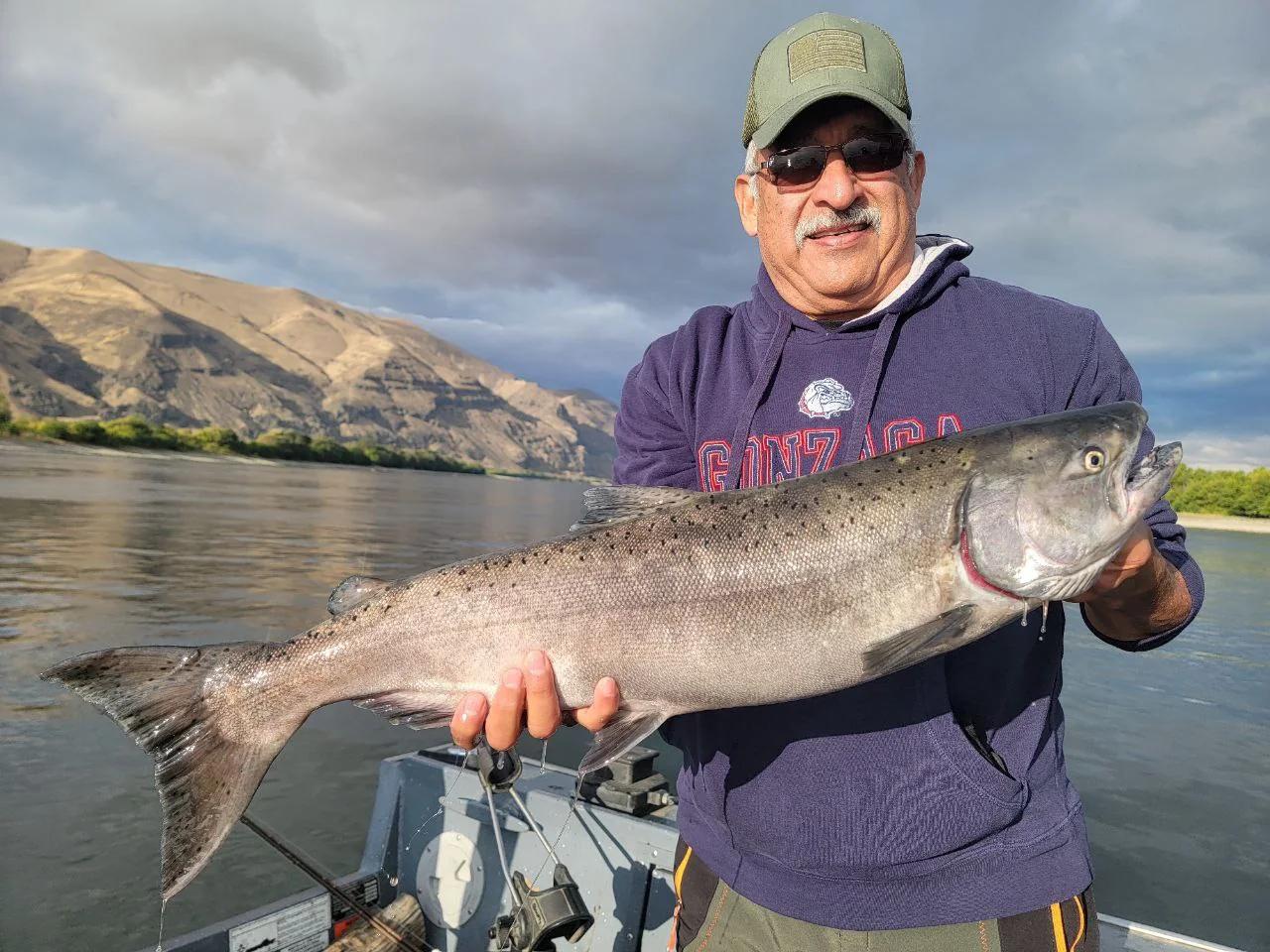 Man in a purple hoodie holding a big Chinook on the river