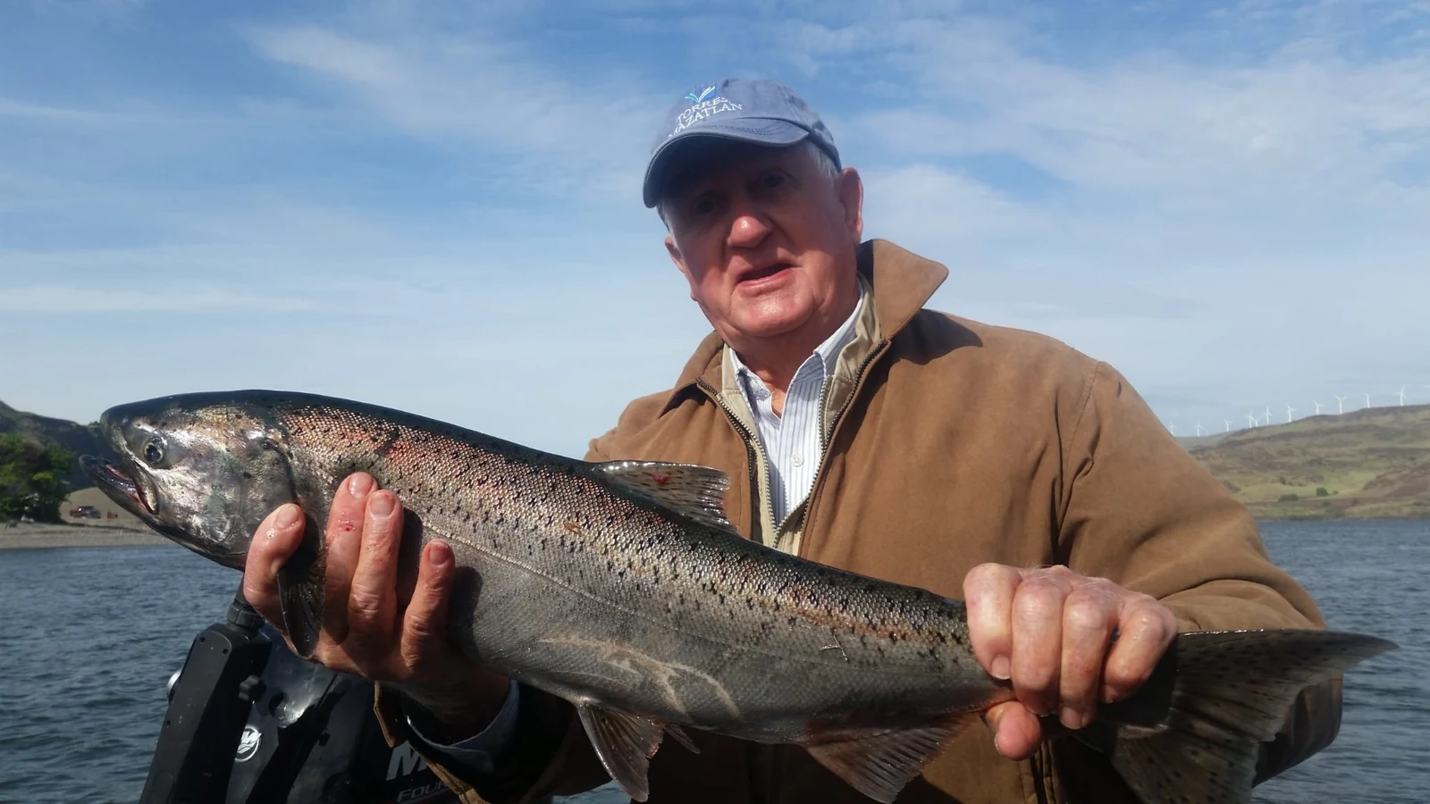 Man in a tan jacket holding a spotted spring Chinook on the river