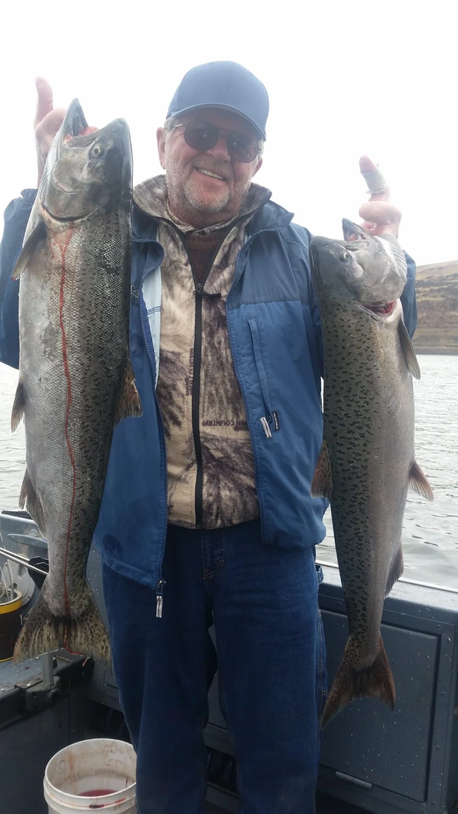 Man in a blue jacket holding two Chinook on the boat
