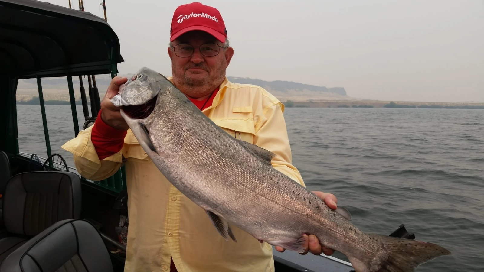 Man in a yellow shirt and red cap holding a silver Chinook on a hazy morning