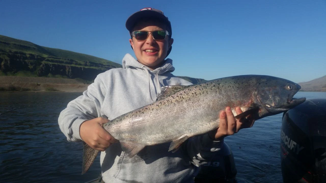 Young angler in a grey hoodie holding a Chinook salmon