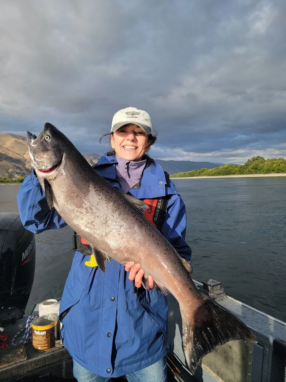 Woman in a blue jacket holding a Chinook salmon on a cloudy day