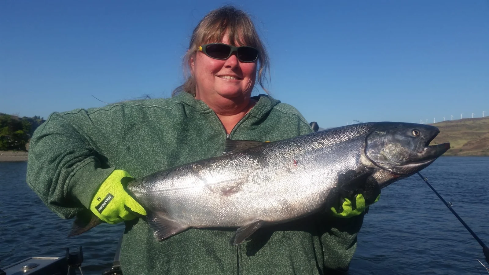 Woman in a green fleece and yellow gloves holding a silver Chinook