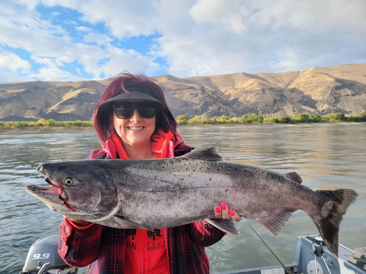 Woman in a red hooded jacket holding a dark Chinook on the river, dry hills behind her