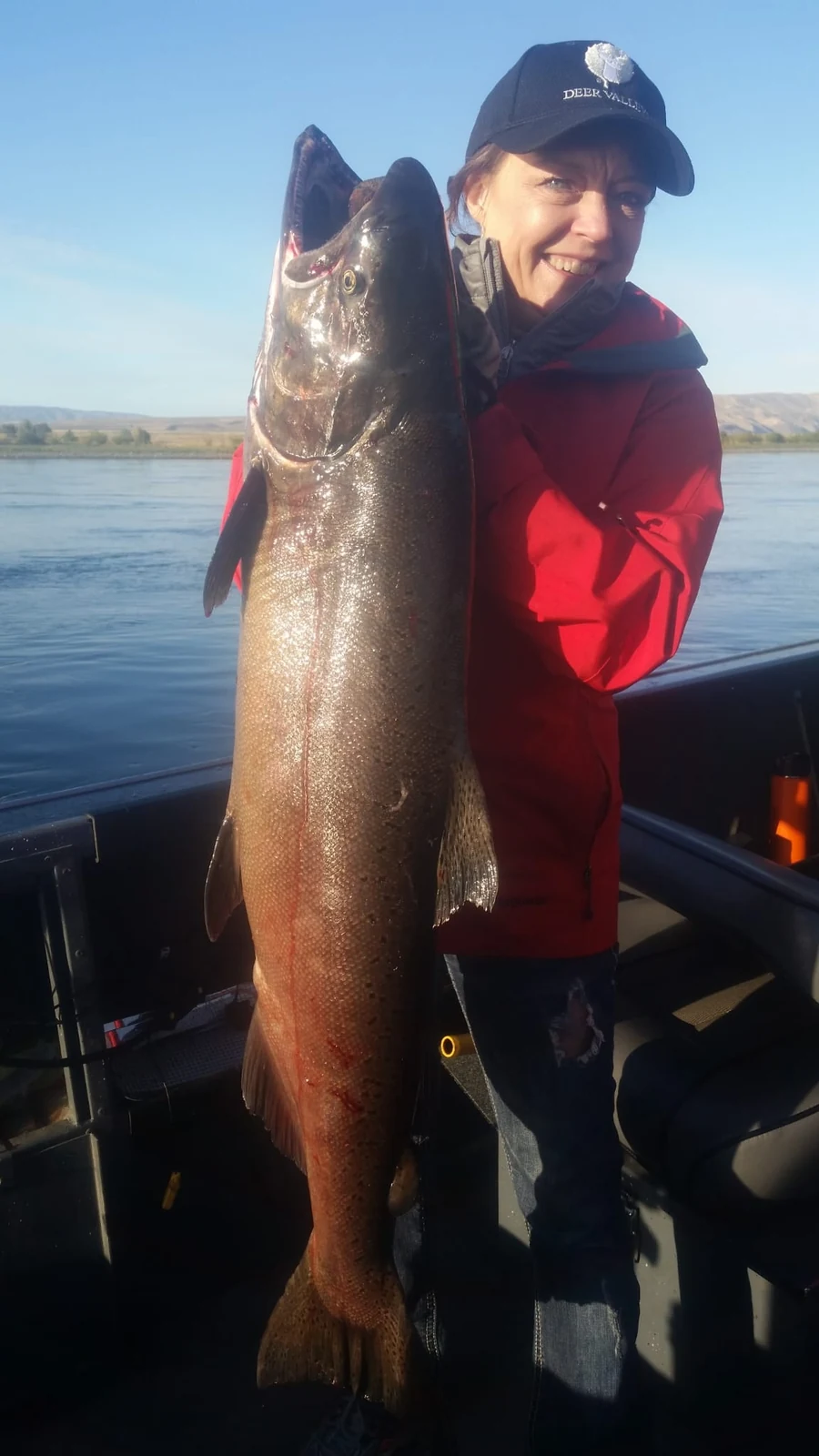 Smiling woman in a red jacket and cap holding a big Chinook