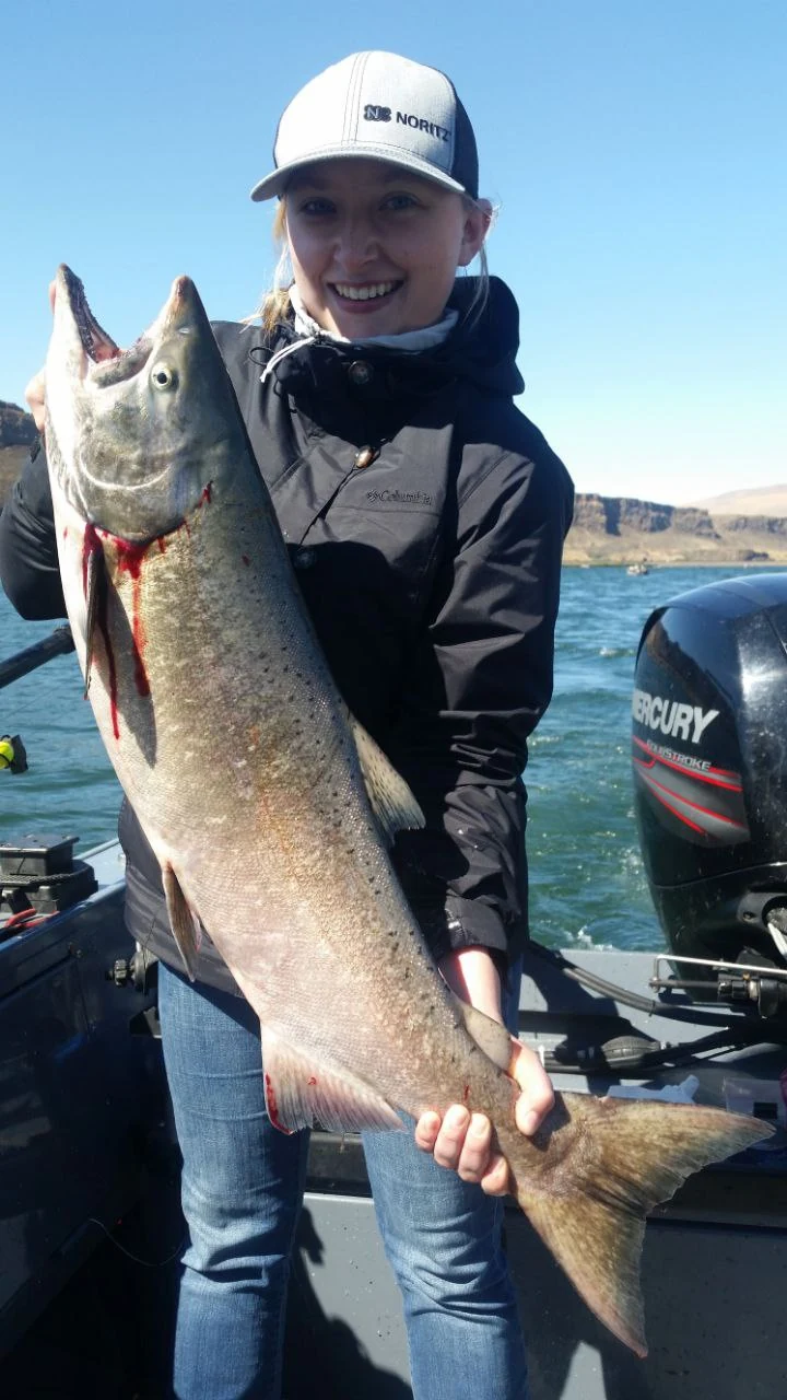 Woman in a white cap holding a big Chinook salmon on the boat