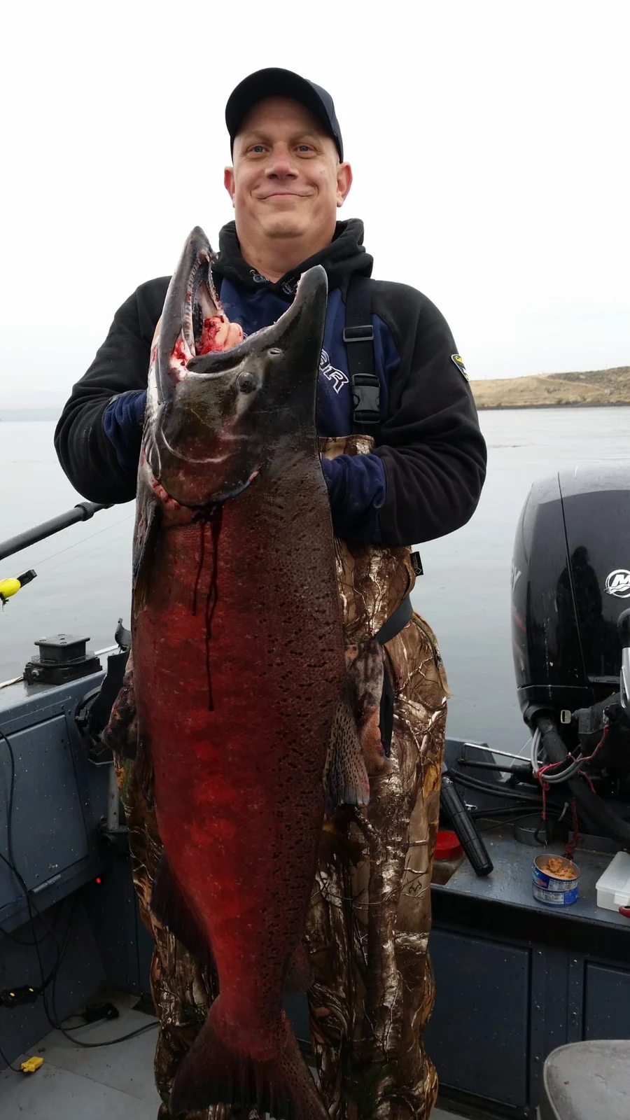 Man in a black jacket holding a big red fall Chinook on the boat