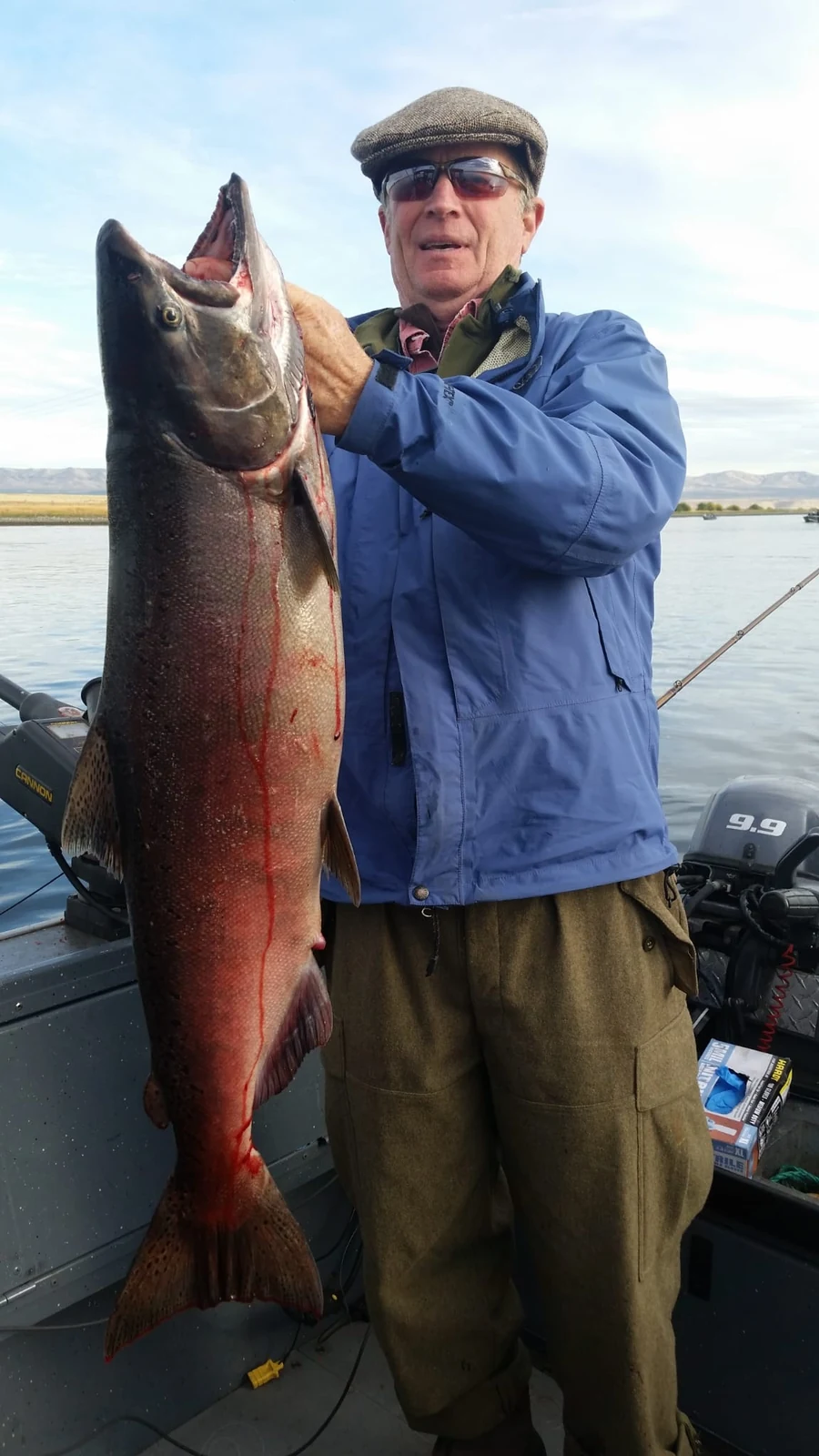 Man in a blue jacket holding a big red fall Chinook on the boat