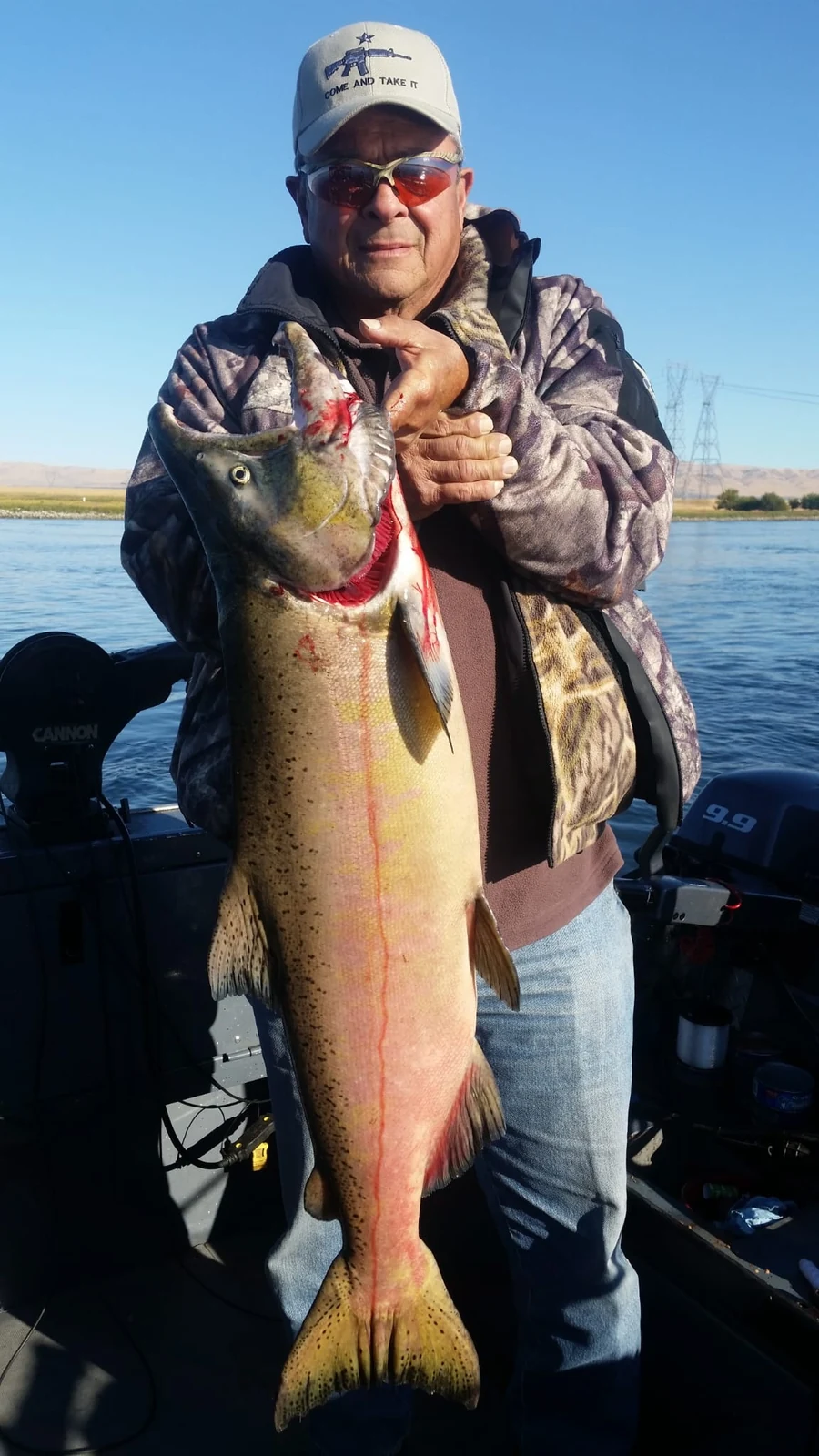 Man in a camouflage hoodie holding a big Chinook on the boat