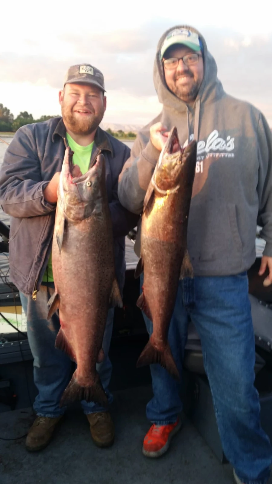 Two anglers each holding a fall Chinook on the boat