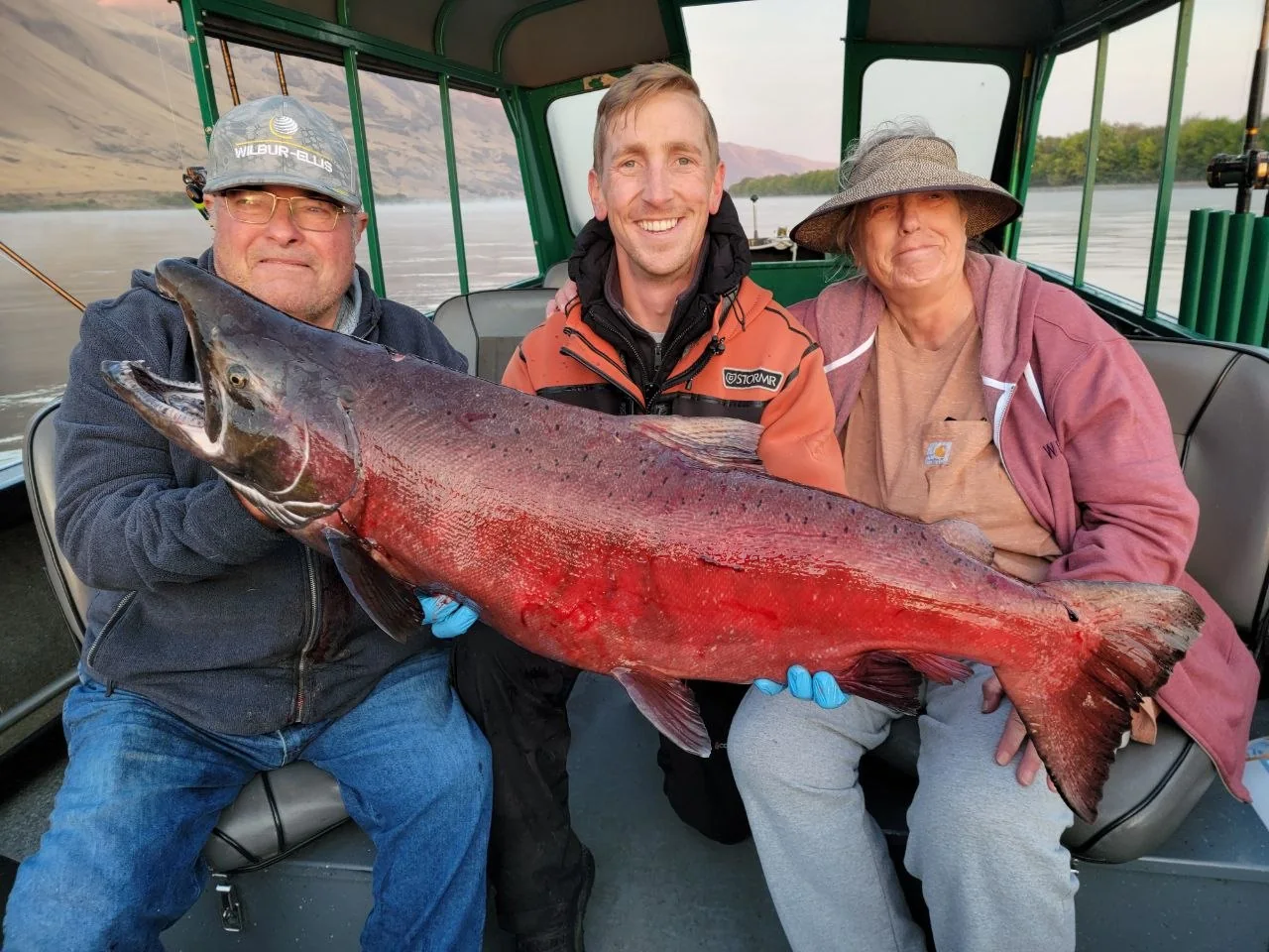 Three anglers on the boat holding red spawning-colour Chinook salmon