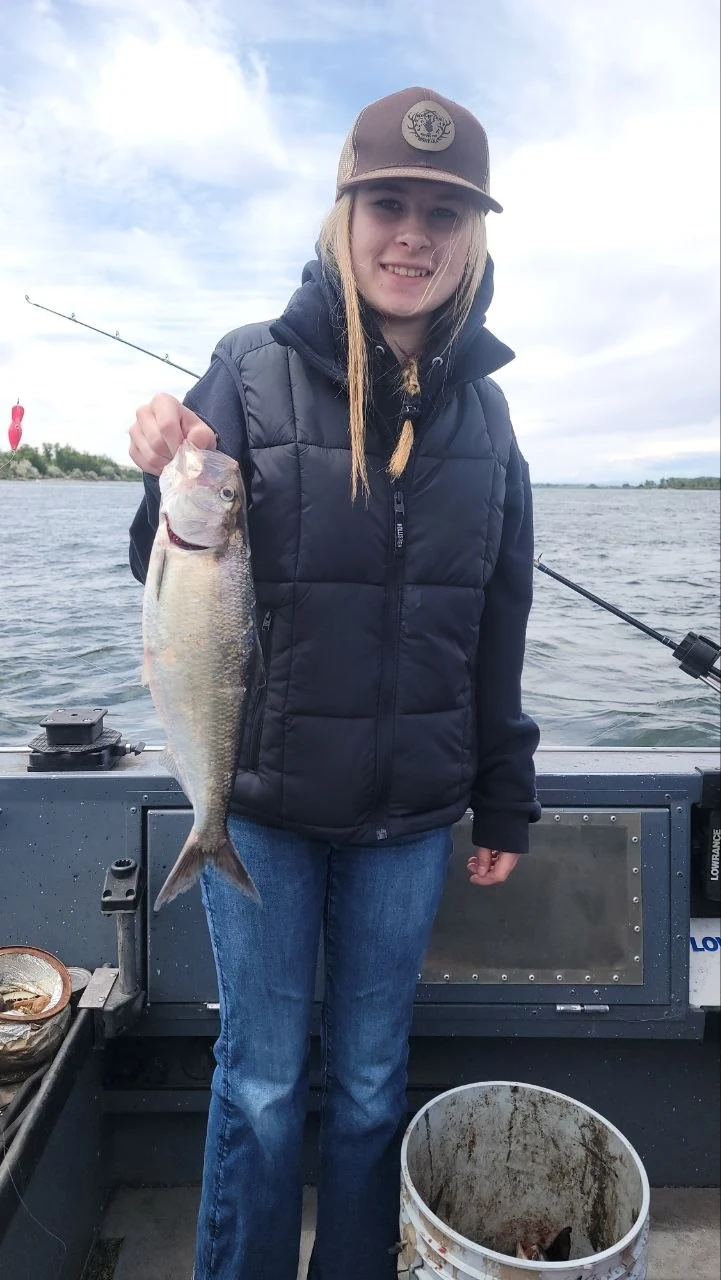 Young angler in a dark jacket holding a shad on the boat
