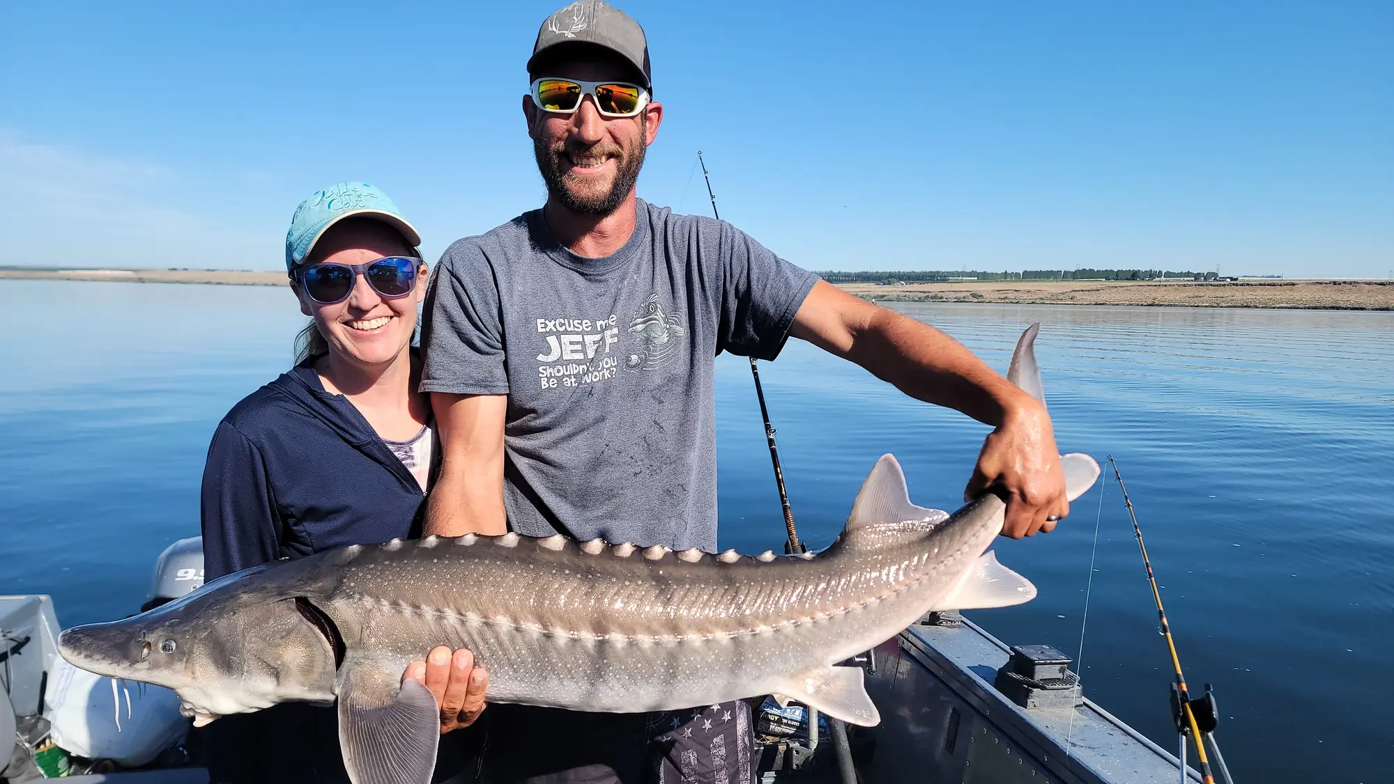 Man and woman on the boat holding a long keeper sturgeon over blue water