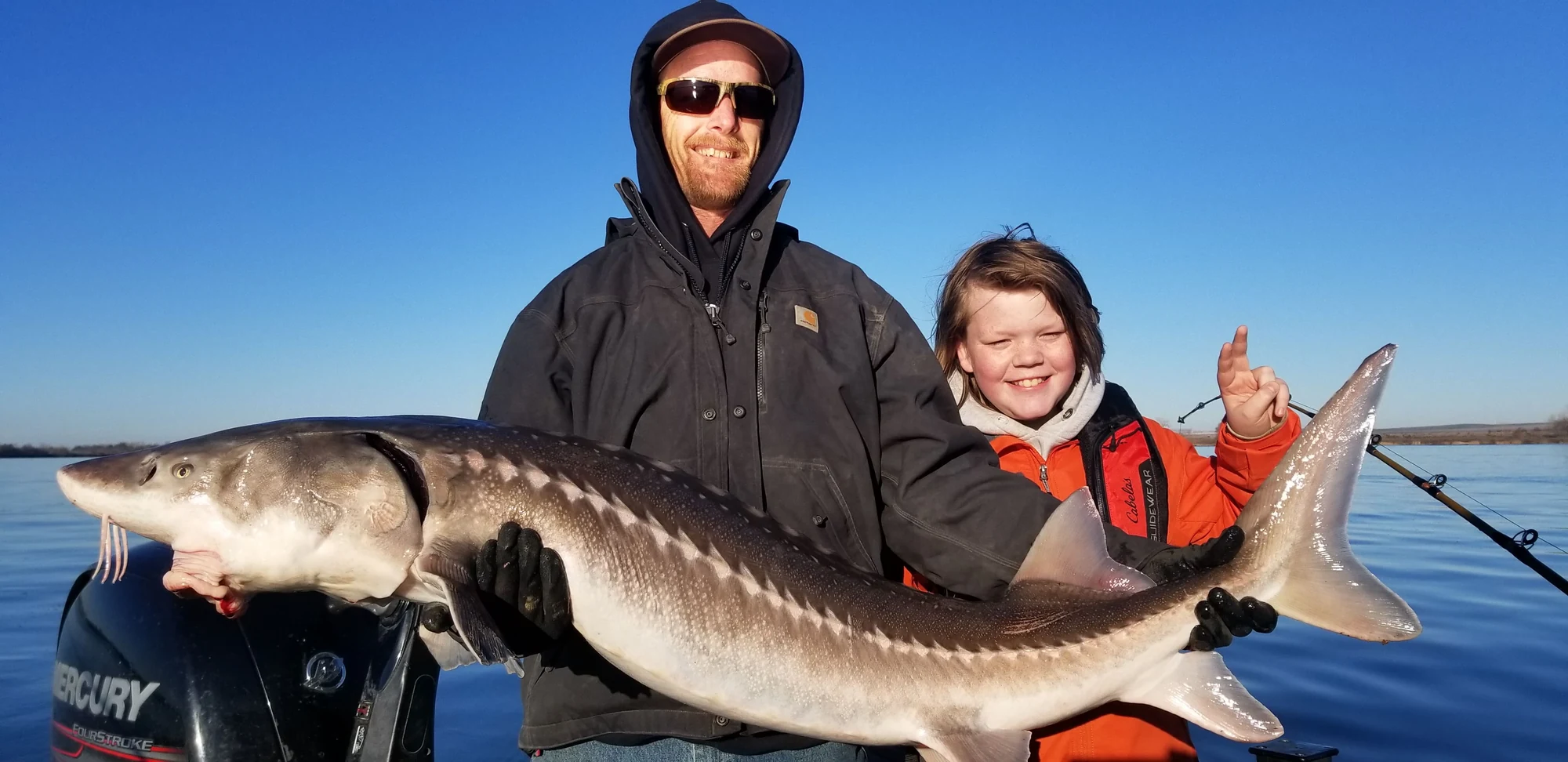 Father and son with a keeper sturgeon on the boat