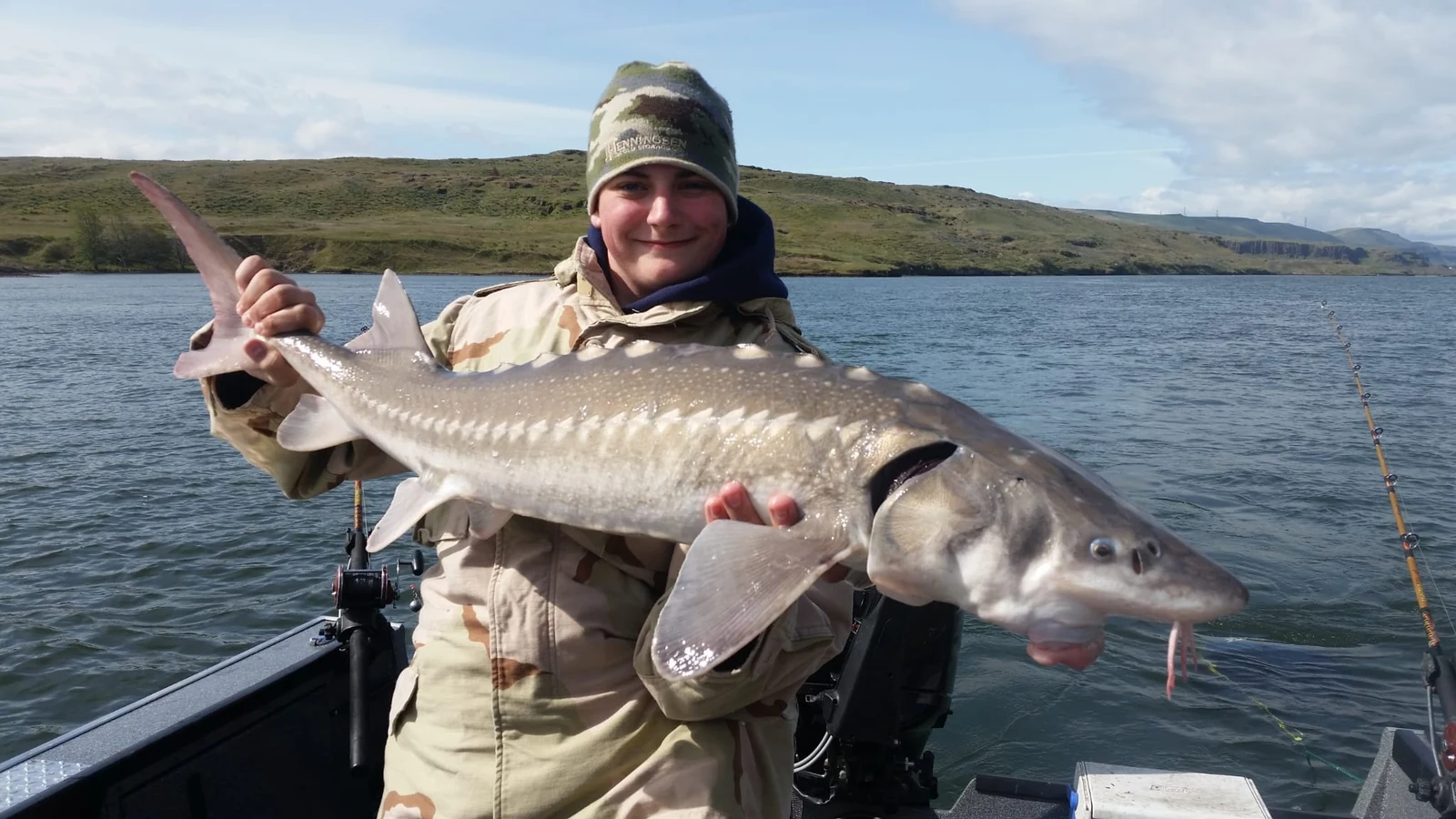 Angler in camouflage and a bucket hat holding a keeper sturgeon