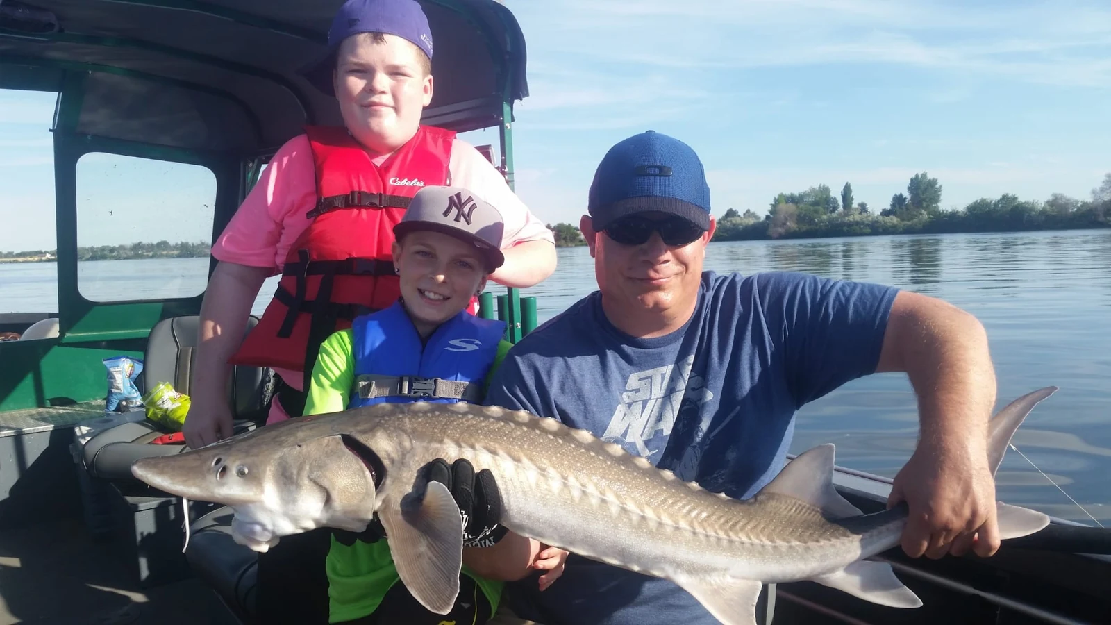 Man and two boys holding a keeper sturgeon inside the cabin boat