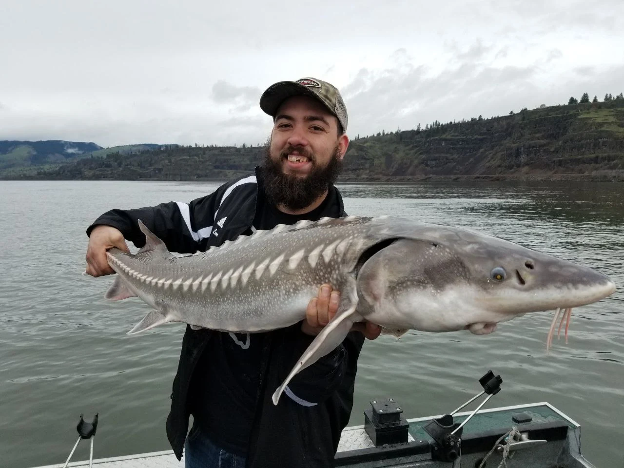 Bearded angler holding a keeper sturgeon under a cloudy sky