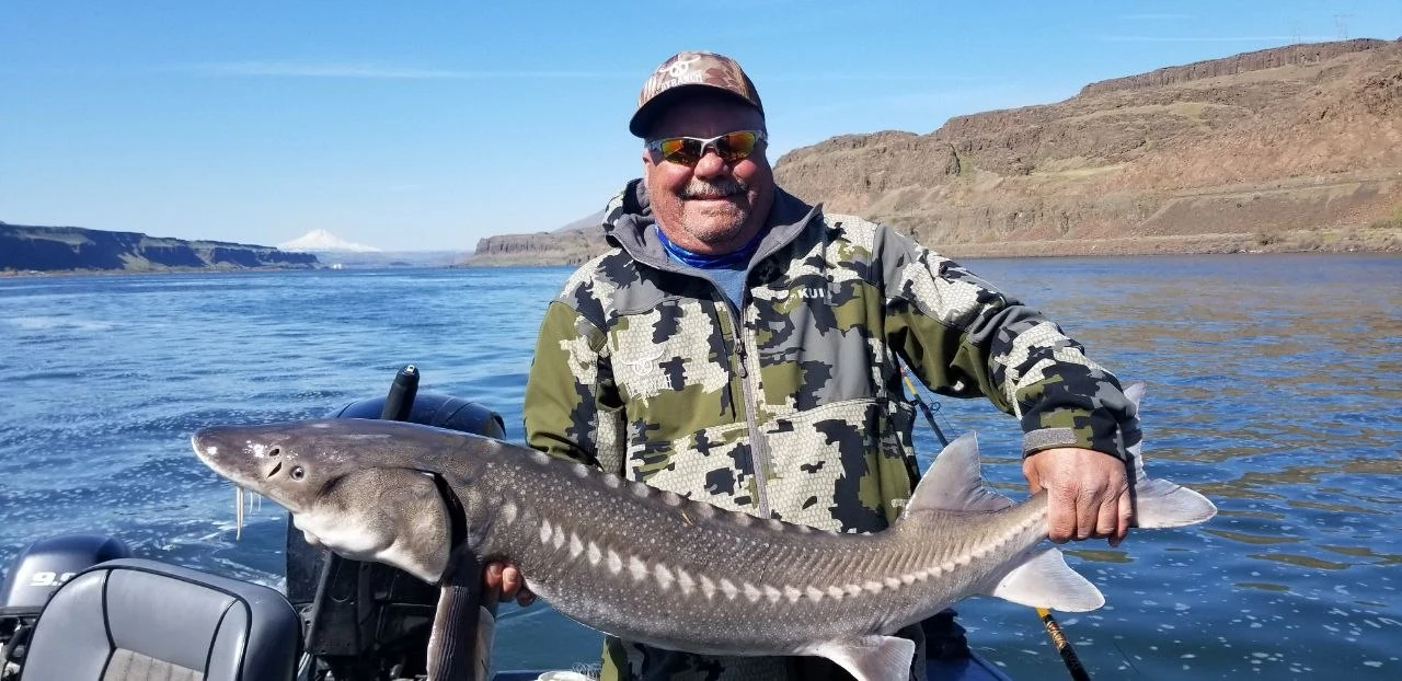 Smiling angler in camouflage holding a keeper sturgeon over blue water