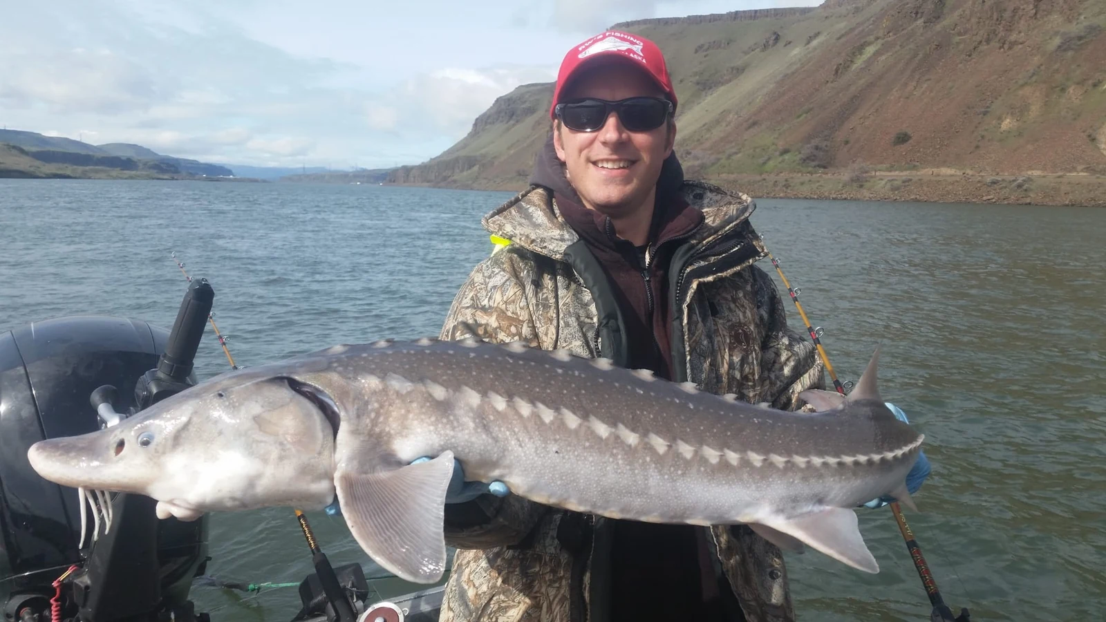 Man in camouflage and a red cap holding a keeper sturgeon