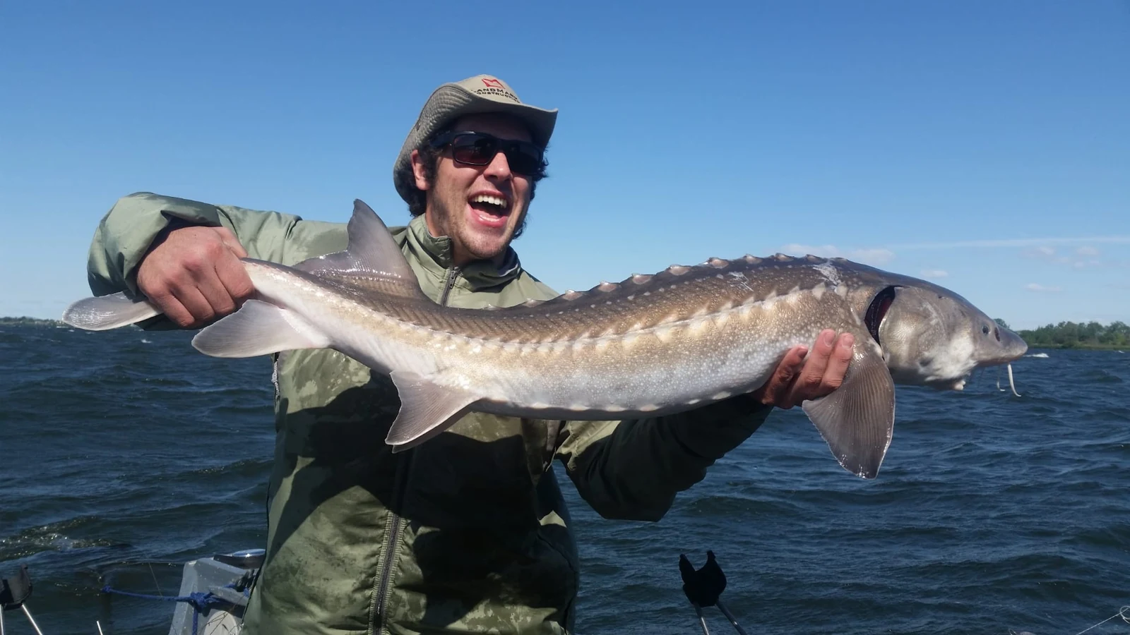 Laughing angler in a bucket hat holding a keeper sturgeon