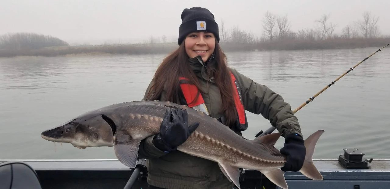 Woman in a life jacket holding a keeper sturgeon on a foggy morning