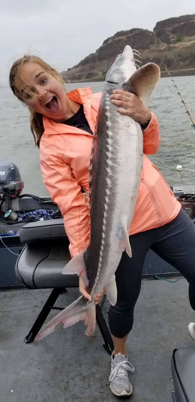 Woman in an orange jacket laughing as she holds up a keeper sturgeon