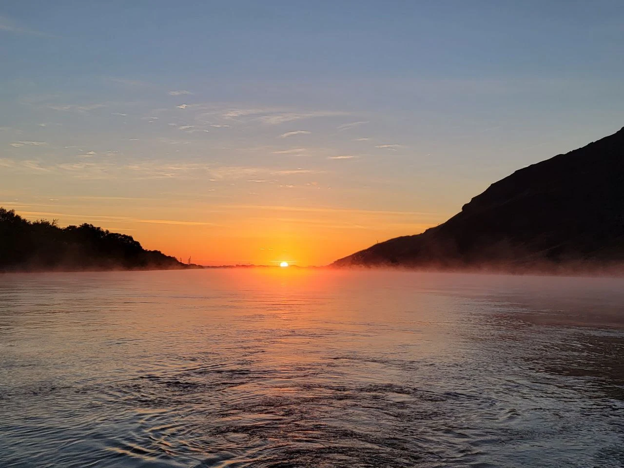 Orange sun rising over the basalt wall of the Columbia River Gorge, glowing on calm water.