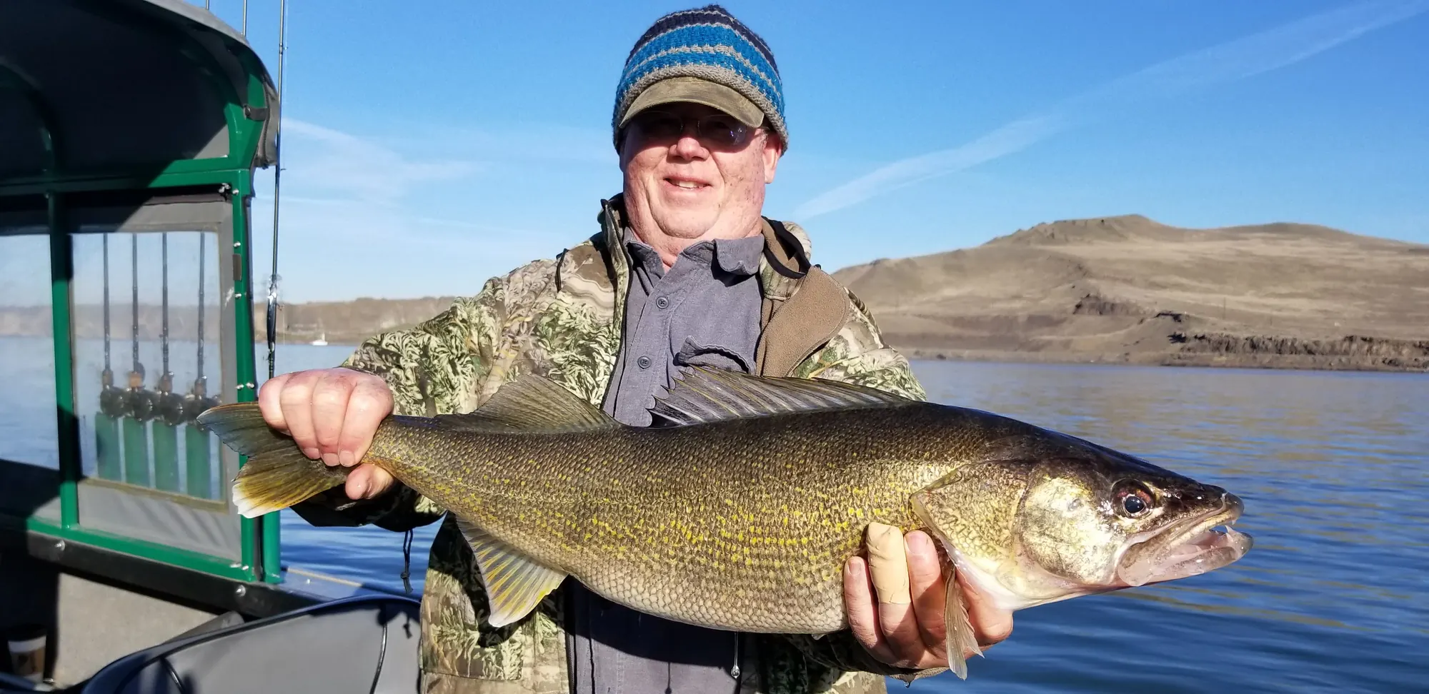 Angler in a striped beanie holding a walleye on the Columbia River