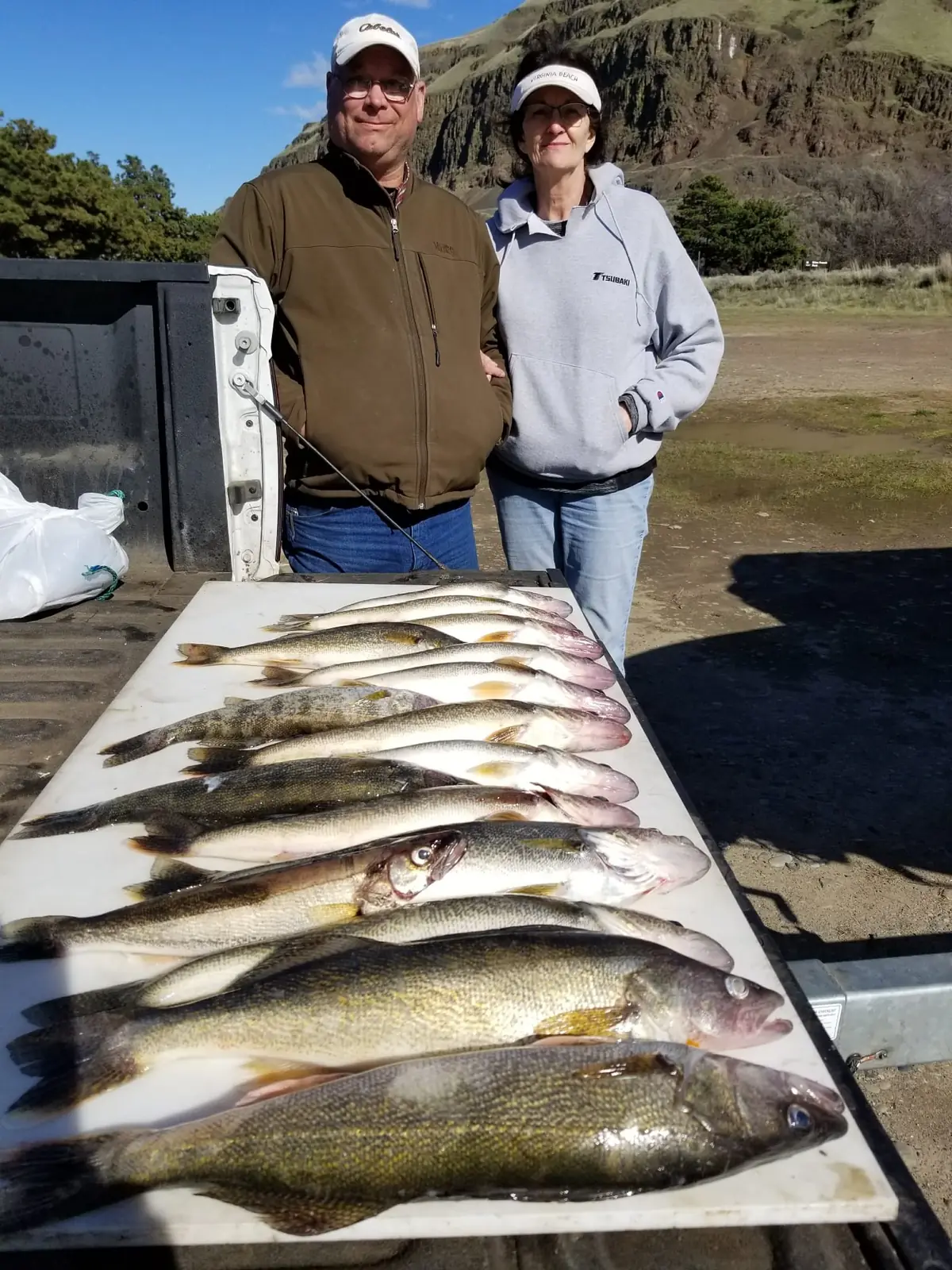 Couple behind a white table of walleye with basalt cliffs behind them