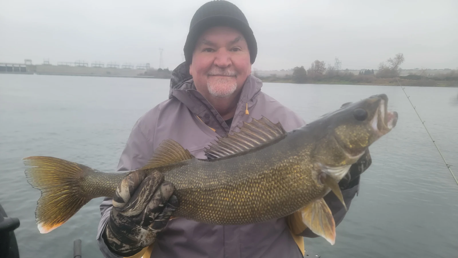 Angler in a beanie holding a walleye on a foggy Columbia River morning