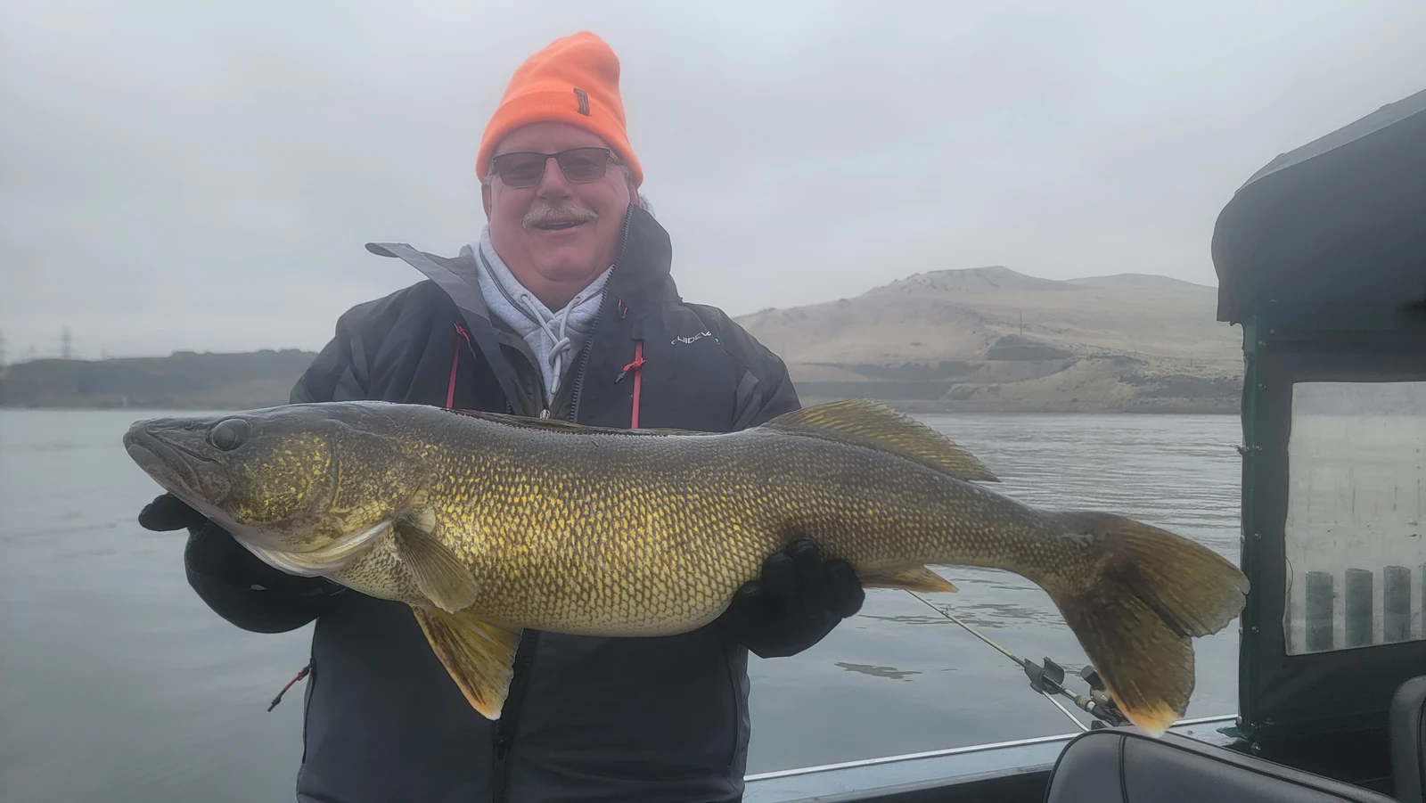 Angler in an orange beanie holding a big walleye in the boat cabin