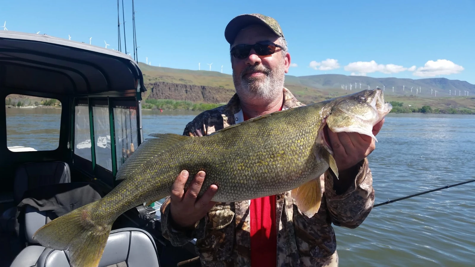 Man in camouflage holding a big walleye beside the windows of the enclosed cabin