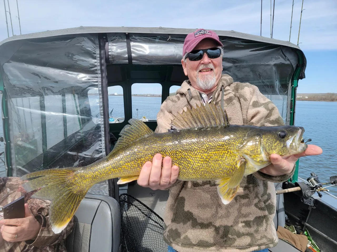 Angler in a red cap holding a big walleye inside the covered cabin of the guide boat