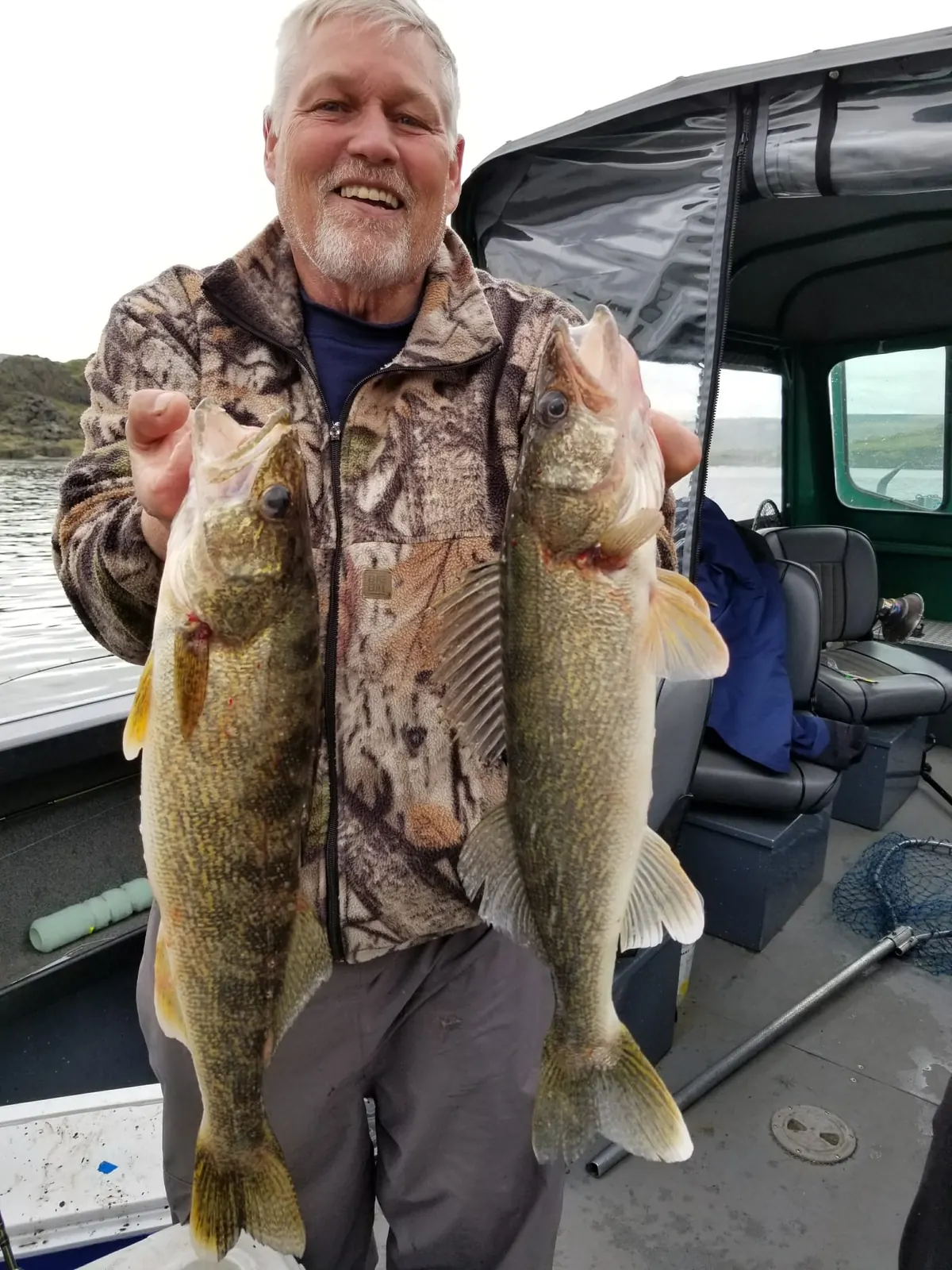 Man in camouflage holding two walleye in the cabin boat