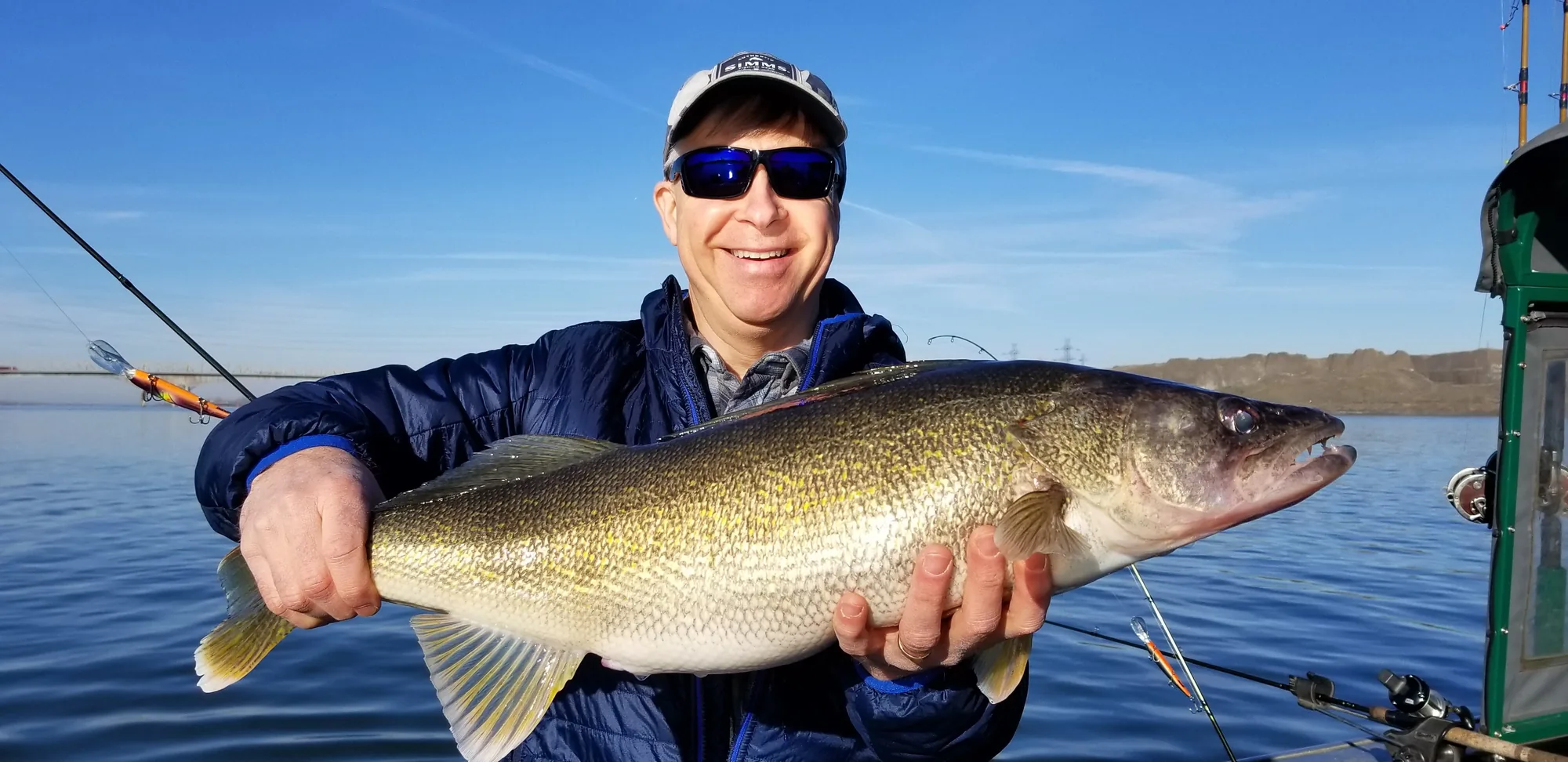 Angler in a blue jacket and sunglasses holding a trophy walleye