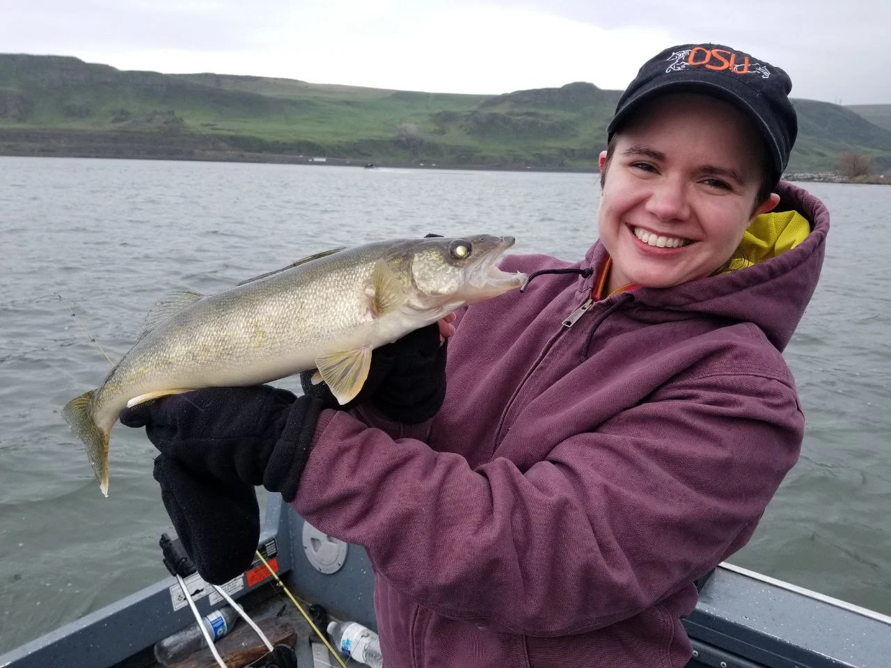 Smiling woman in a maroon hoodie and cap holding a walleye